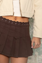 Woman wearing TIC TOC SG31603-DUSTY DUSTY western lace-up pleated skort featuring a western-inspired lace-up eyelet waistband, mid rise mini length, structured pleated denim silhouette with side zipper closure, and built-in soft inner shorts, styled with a fitted top and western boots for a festival-ready everyday western look.