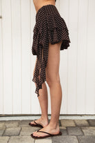 Woman wearing BISCOTTI polka dot chiffon ruffle skirt featuring a tiered mini skirt silhouette, asymmetrical dropped ruffle side detail, side zipper closure, built-in shorts lining, and a lightweight flowy hem for coquette summer and resort styling.