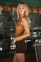 Woman in a brown sleeveless top and shorts standing in front of a glass wall.