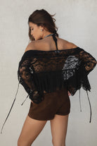 Woman wearing a black lace top and brown shorts against a plain background