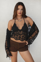 Woman wearing a black lace top and brown shorts against a white background