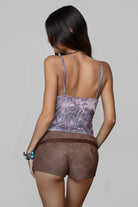 Woman wearing a patterned top and brown shorts on a plain background