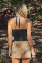 Person wearing a black halter top with studded details and a beige skirt outdoors.