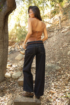 Woman wearing TIC TOC SIENNA Faux Suede Halter Bustier Top in tan with exposed eyelet lace detail and deep V neckline for a western festival look paired with denim pants on a forest setting. 