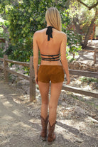 Woman wearing TIC TOC INDIE Split Front Halter Top in black with plunging neckline, studded detailing, and open back with buckle straps and brown suede shorts paired with cowboy boots outdoors. 