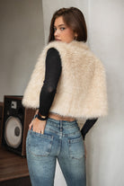 Woman wearing TIC TOC TA31834 BRIENNE faux fur vest in a natural tone; cropped open-front silhouette with plush texture, styled over a long-sleeve top and denim indoors.