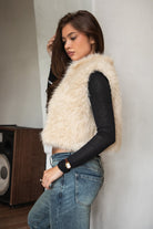 Woman wearing TIC TOC TA31834 BRIENNE faux fur vest in a natural tone; cropped open-front silhouette with plush texture, styled over a long-sleeve top and denim indoors.