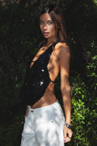 Woman wearing TIC TOC TA31927 CELESTIA matte sequin halter top featuring allover matte sequin embellishment, a deep draped cowl neckline, halter neck with adjustable strap, open back with adjustable back strap, and a relaxed flowy silhouette for a statement festival and night-out look.