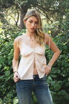 Woman wearing SOIE split V-neck satin cami top featuring scalloped lace trim along the neckline and front panel, adjustable self tie shoulder straps, five button front closure, front split hem detail, and an elastic back band for a soft feminine silhouette.