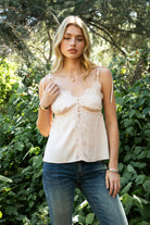 Woman wearing SOIE split V-neck satin cami top featuring scalloped lace trim along the neckline and front panel, adjustable self tie shoulder straps, five button front closure, front split hem detail, and an elastic back band for a soft feminine silhouette.