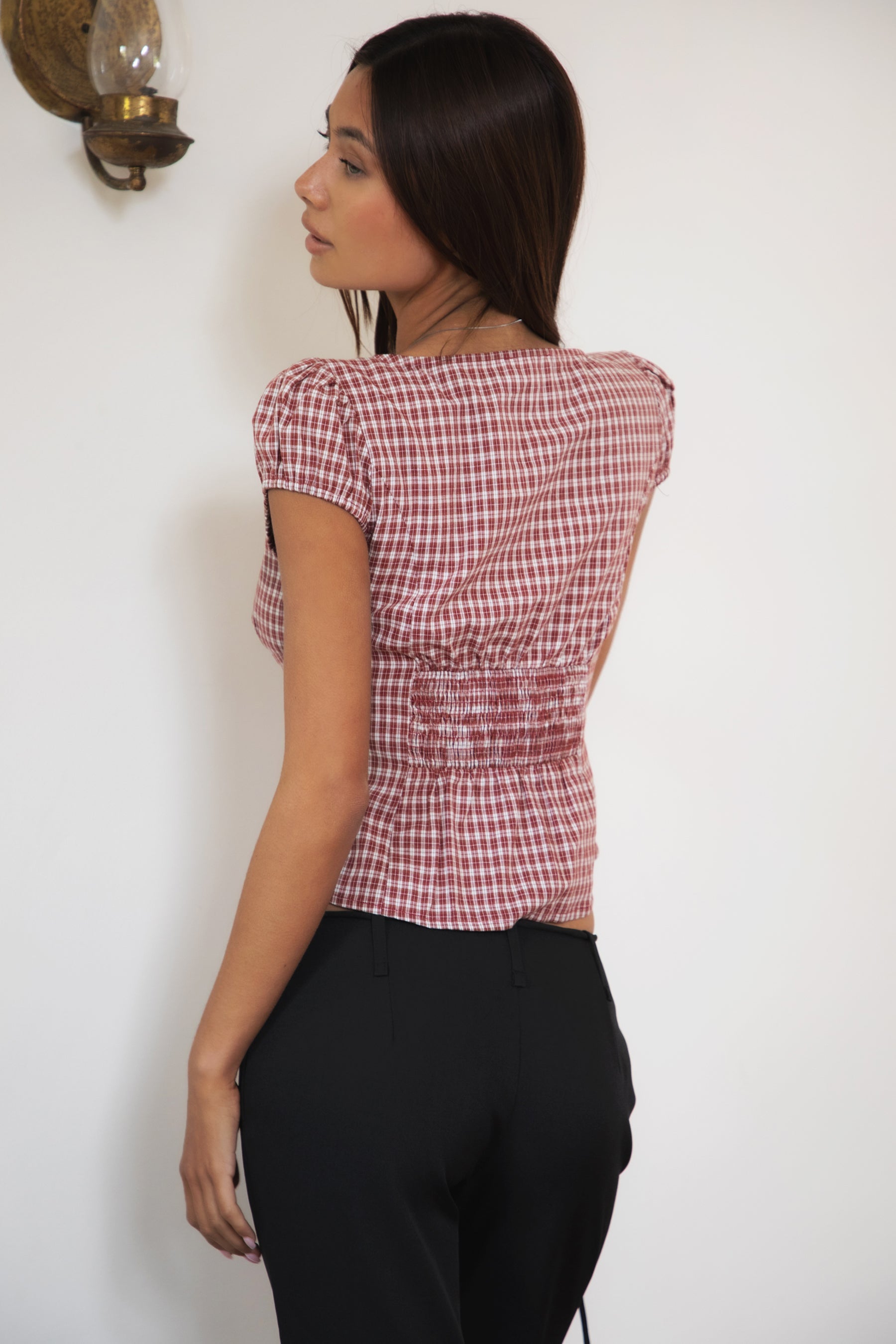 Woman wearing TIC TOC TA32072 DARIS gingham puff sleeve blouse top featuring soft cotton gingham fabric with a classic check pattern, cropped feminine fit, round neckline with front button closure, puff short sleeves, smocked back panel, and under bust smocking for a vintage-inspired western look.