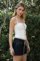 Woman wearing STARLANE sequin lace up halter denim top featuring a clear sequin embroidered front panel, eyelet lace up closure, thin adjustable halter straps, studded trim along the top and hem, and a fitted stretch denim silhouette with back zipper closure and jersey lining.