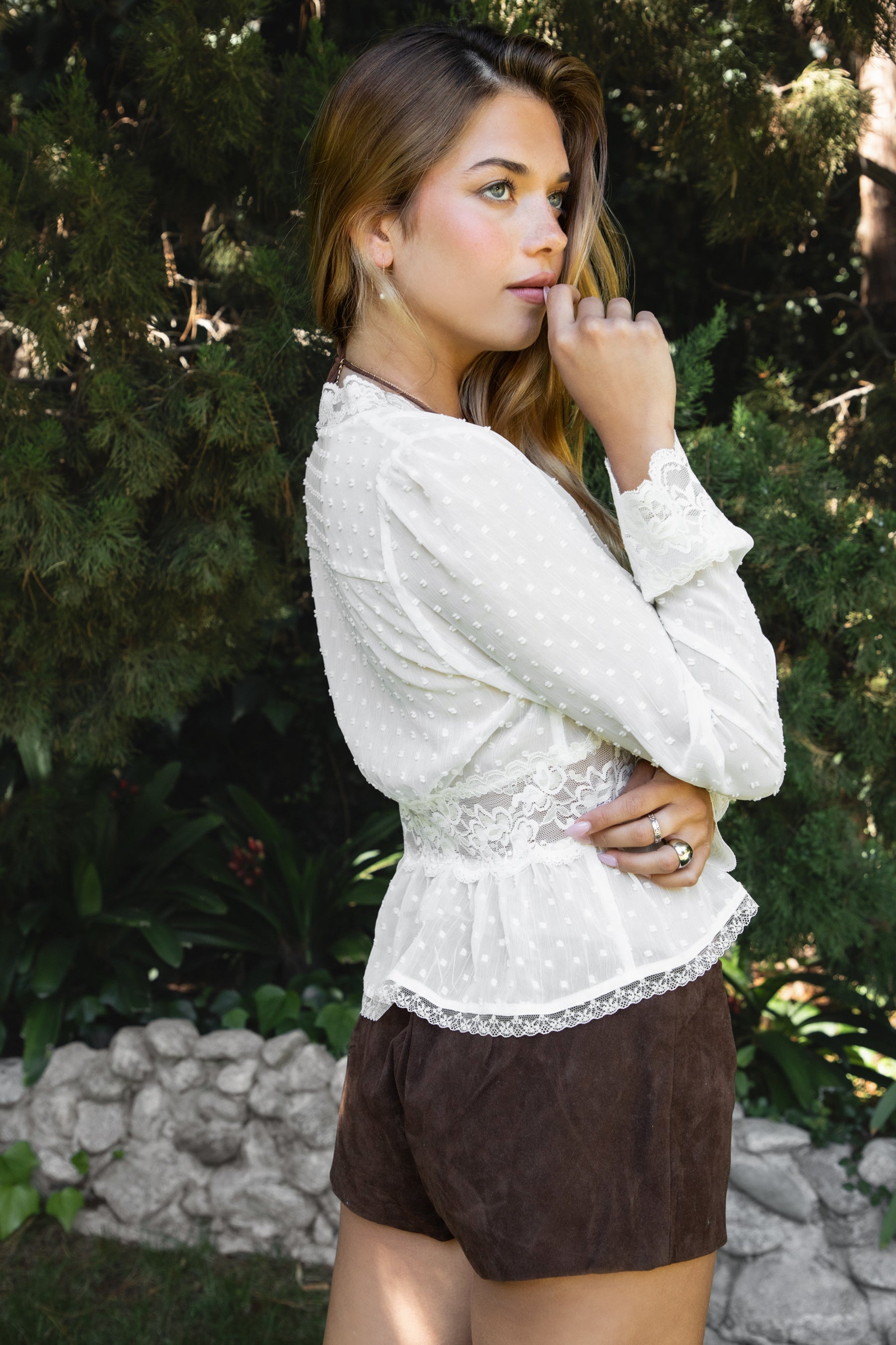Woman wearing LACEWOOD polka dot chiffon lace long sleeve blouse top featuring sheer dotted chiffon fabric, scalloped lace trim along the V-neckline and cuffs, floral lace panel under the bust, flowy silhouette with flare hem, and front button closure for adjustable styling