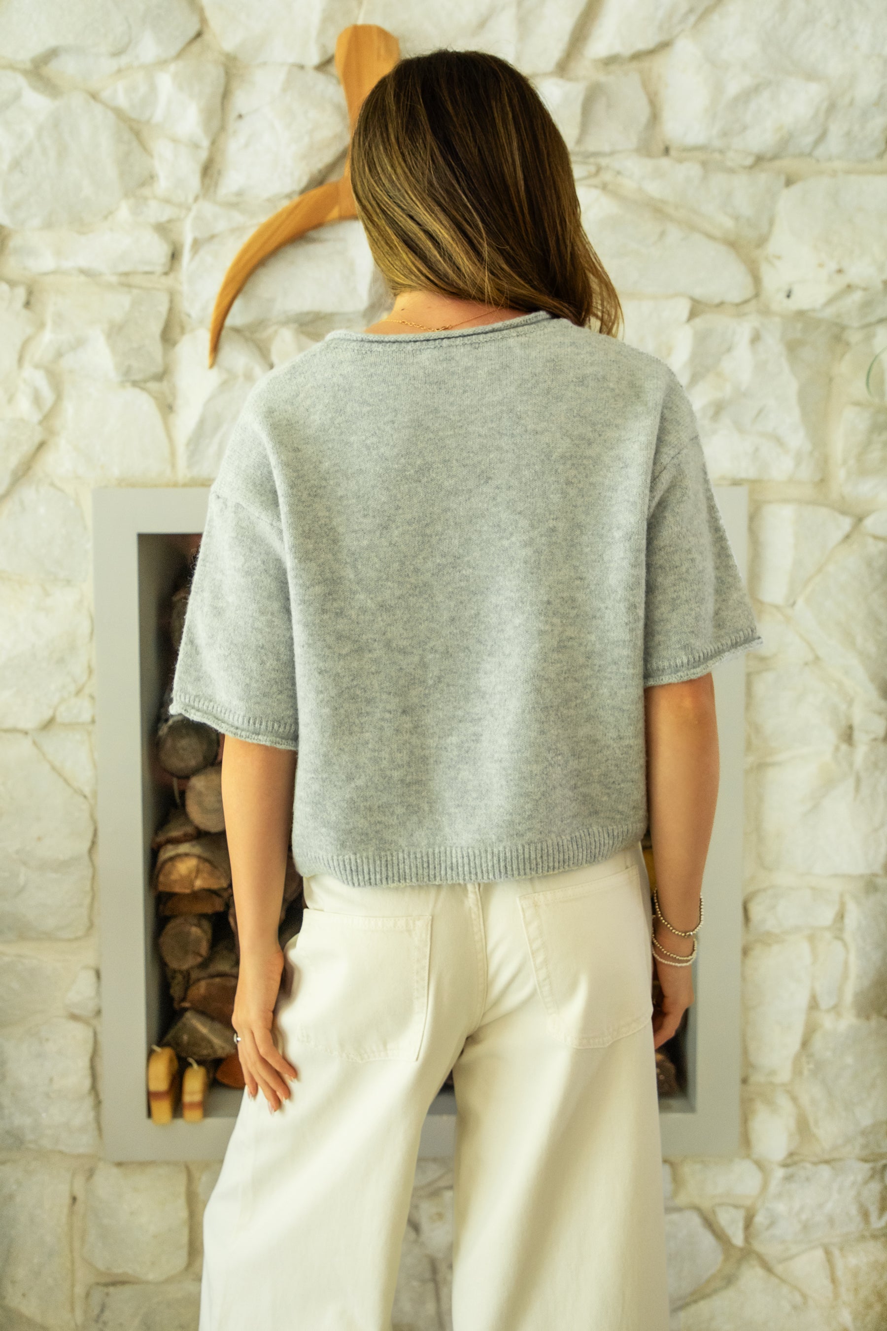 Woman wearing HOLLIS roll neck drop shoulder short sleeve knit sweater featuring a minimal rolled neckline, relaxed semi oversized silhouette, short sleeves with rolled cuffs, ribbed hem, front marbled button closure, and lightweight cotton knit for everyday layering.