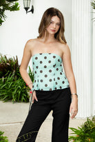 Woman wearing DULCIE polka dot convertible scarf tube top featuring a playful polka dot print, structured strapless silhouette, matching convertible scarf, smocked back panel, side zipper, and paneled bodice with subtle peplum hem for vacation and resort styling.