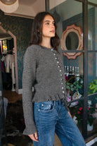 Woman wearing FRILLIA ruffle trim button front knit cardigan featuring soft brushed sweater knit fabric, cozy stretch feel, round neckline, button front closure, delicate ruffle trim along the front placket and hem, long sleeves with flared ruffle cuffs, and relaxed cropped silhouette.