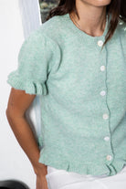 Woman wearing ELSSEE soft ruffle trim button down knit cardigan featuring soft brushed sweater knit fabric, classic crew neckline, button front closure, short puff sleeves with delicate ruffle cuffs, ruffle trim hem, and a cozy cropped silhouette for everyday layering.