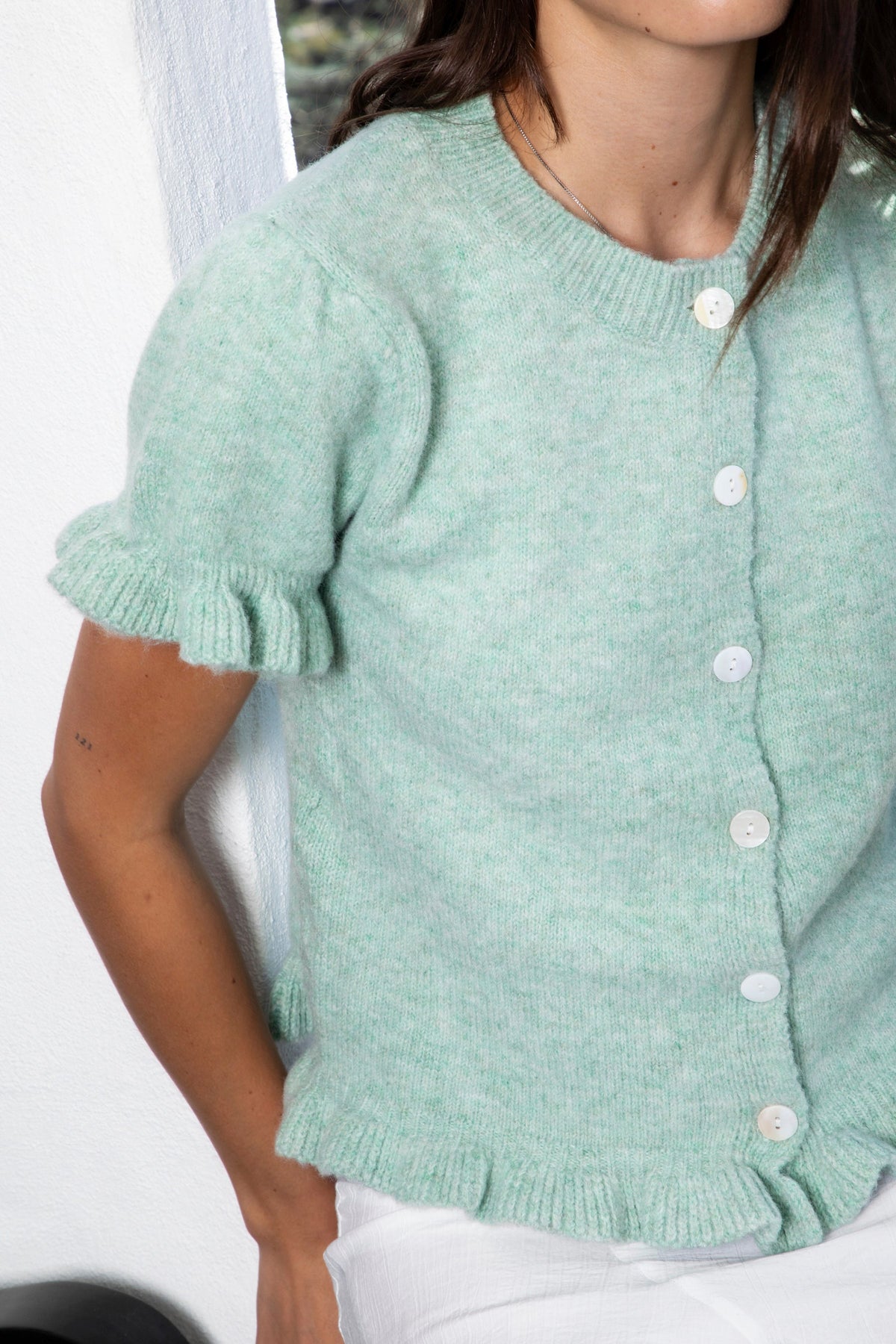 Woman wearing ELSSEE soft ruffle trim button down knit cardigan featuring soft brushed sweater knit fabric, classic crew neckline, button front closure, short puff sleeves with delicate ruffle cuffs, ruffle trim hem, and a cozy cropped silhouette for everyday layering.