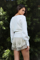 Woman wearing ADEL surplice V neck knit sweater top featuring soft marled sweater knit fabric with a cozy feel, deep V neckline, surplice wrap front design, overlapping front panels, relaxed drop shoulders, long balloon sleeves with fitted ribbed cuffs, wide ribbed waistband, slightly cropped length, and blouson fit.