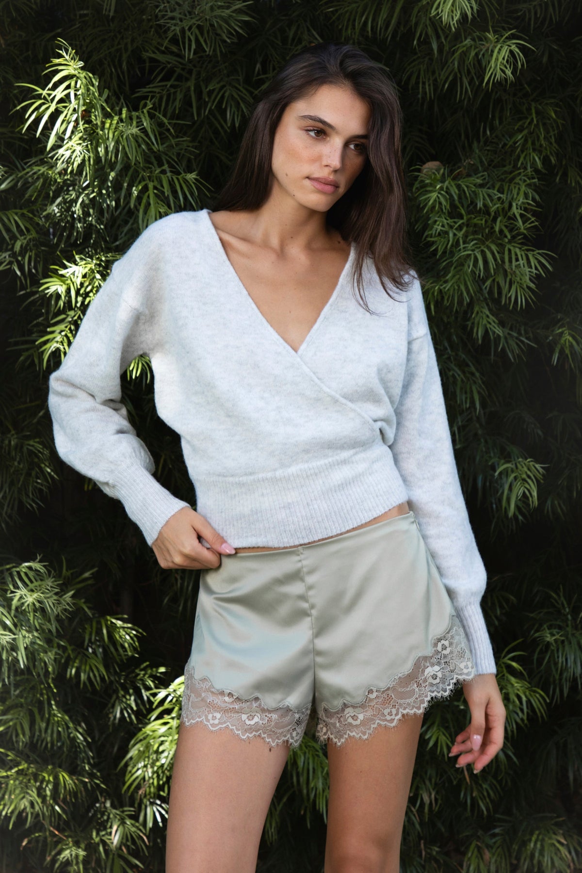 Woman wearing ADEL surplice V neck knit sweater top featuring soft marled sweater knit fabric with a cozy feel, deep V neckline, surplice wrap front design, overlapping front panels, relaxed drop shoulders, long balloon sleeves with fitted ribbed cuffs, wide ribbed waistband, slightly cropped length, and blouson fit.