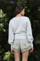 Woman wearing ADEL surplice V neck knit sweater top featuring soft marled sweater knit fabric with a cozy feel, deep V neckline, surplice wrap front design, overlapping front panels, relaxed drop shoulders, long balloon sleeves with fitted ribbed cuffs, wide ribbed waistband, slightly cropped length, and blouson fit.