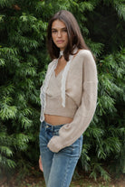Woman wearing ADEL surplice V neck knit sweater top featuring soft marled sweater knit fabric with a cozy feel, deep V neckline, surplice wrap front design, overlapping front panels, relaxed drop shoulders, long balloon sleeves with fitted ribbed cuffs, wide ribbed waistband, slightly cropped length, and blouson fit.