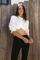 Woman wearing MAIZY eyelet trim cropped three quarter sleeve poplin blouse featuring lightweight cotton poplin fabric, romantic high ruffle neckline, delicate eyelet lace trim, open front cropped silhouette, voluminous puff sleeves, elastic ruffle cuffs, and elasticized hem for feminine styling.