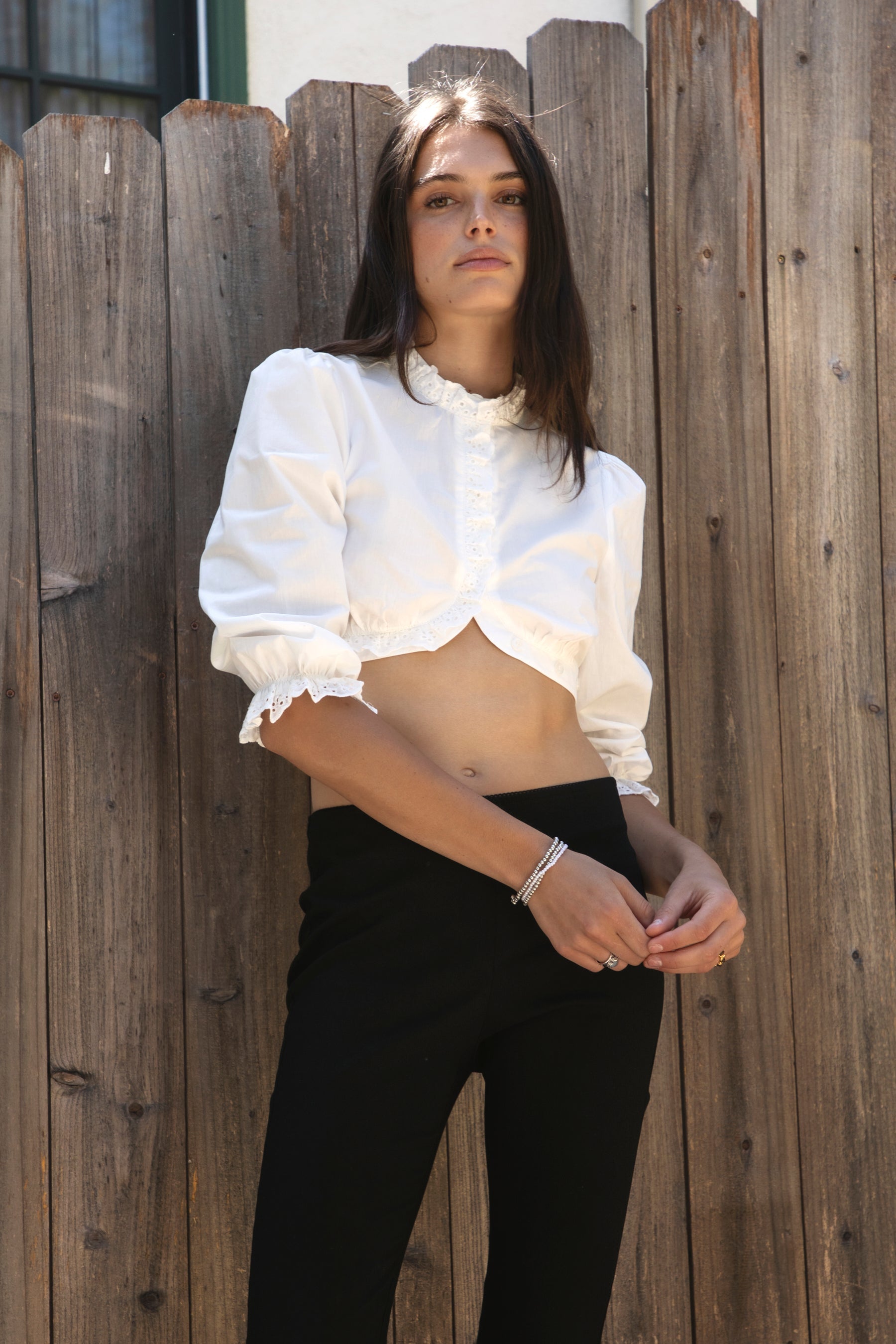Woman wearing MAIZY eyelet trim cropped three quarter sleeve poplin blouse featuring lightweight cotton poplin fabric, romantic high ruffle neckline, delicate eyelet lace trim, open front cropped silhouette, voluminous puff sleeves, elastic ruffle cuffs, and elasticized hem for feminine styling.