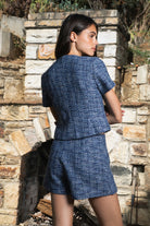 Woman wearing COCO navy blue lurex tweed short sleeve top featuring shimmering textured tweed fabric, subtle metallic lurex detail, round neckline, fitted structured bodice, cropped length, elegant gold point buttons, decorative faux chest pockets, and fully lined construction designed to coordinate with the matching COCO skort.