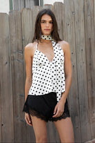 Woman wearing LUCETTE polka dot satin halter top featuring soft satin fabric, classic polka dot print, deep V neckline, flowy babydoll silhouette, adjustable self tie halter scarf neck detail, open back, and elasticized back for comfortable going out styling.