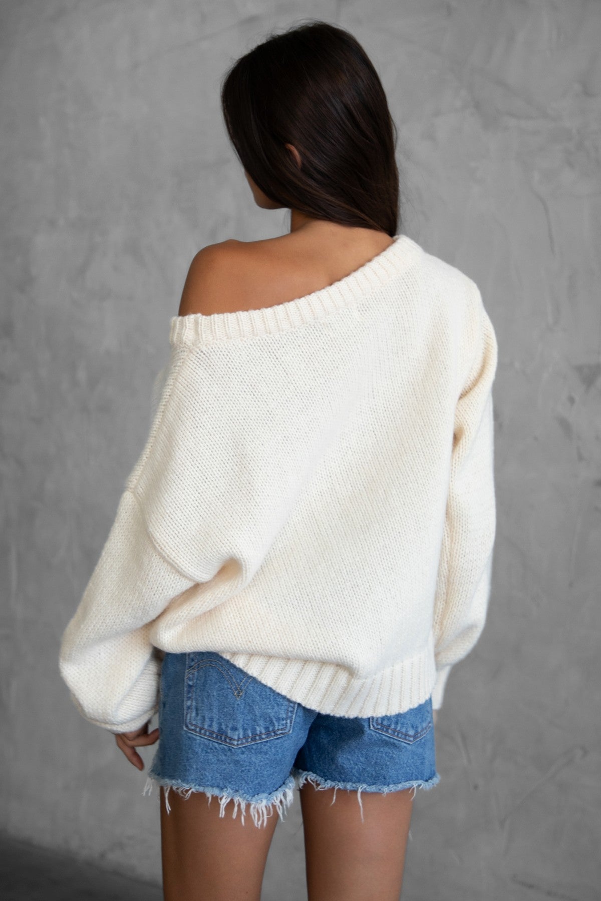 Woman wearing a TIC TOC BRANDI Ribbed Knit Sweater in cream with off-the-shoulder boat neck, American flag pattern, and semi-oversized fit, paired with denim blue shorts.