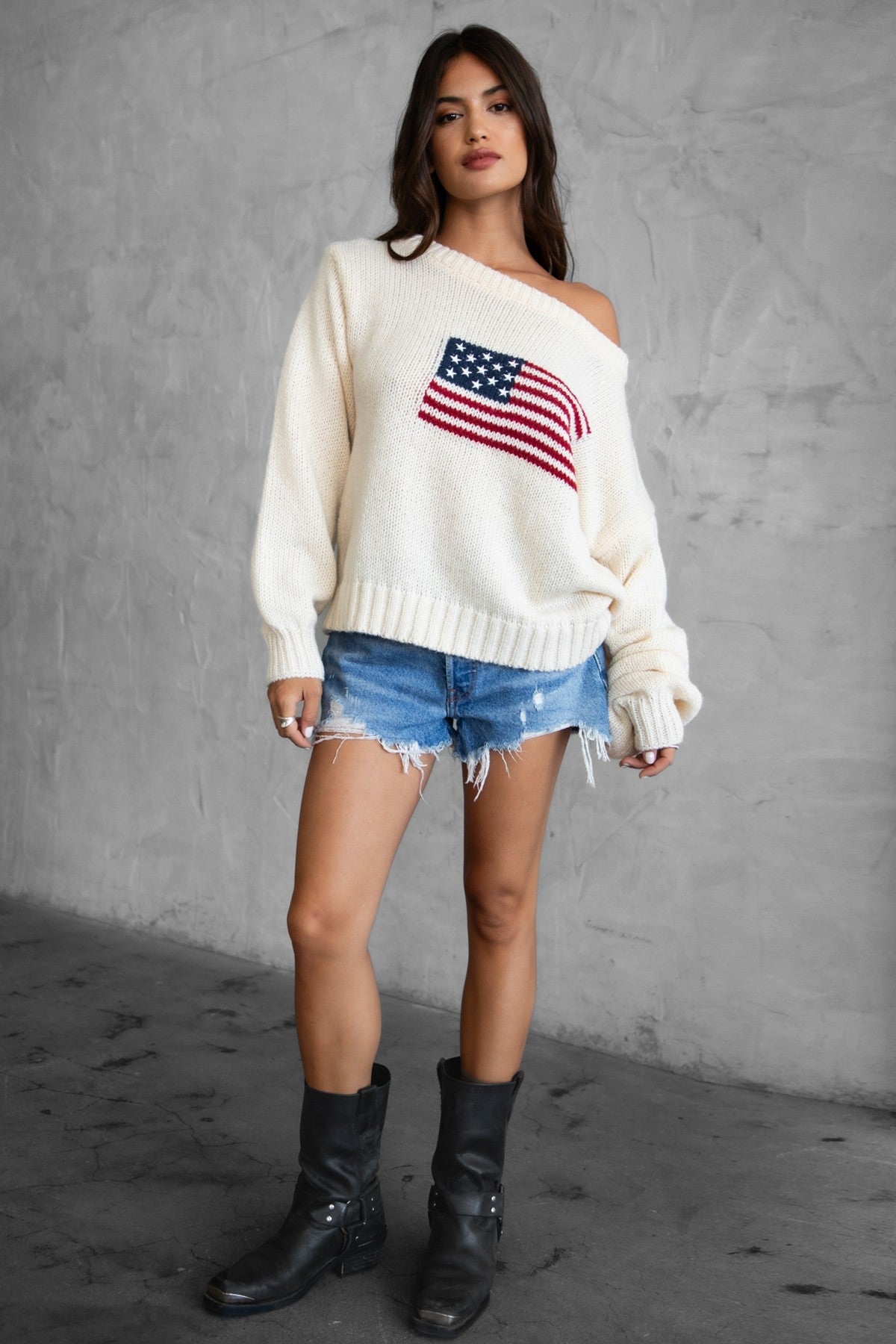 Woman wearing a TIC TOC BRANDI Ribbed Knit Sweater in cream with off-the-shoulder boat neck, American flag pattern, and semi-oversized fit, paired with denim blue shorts.