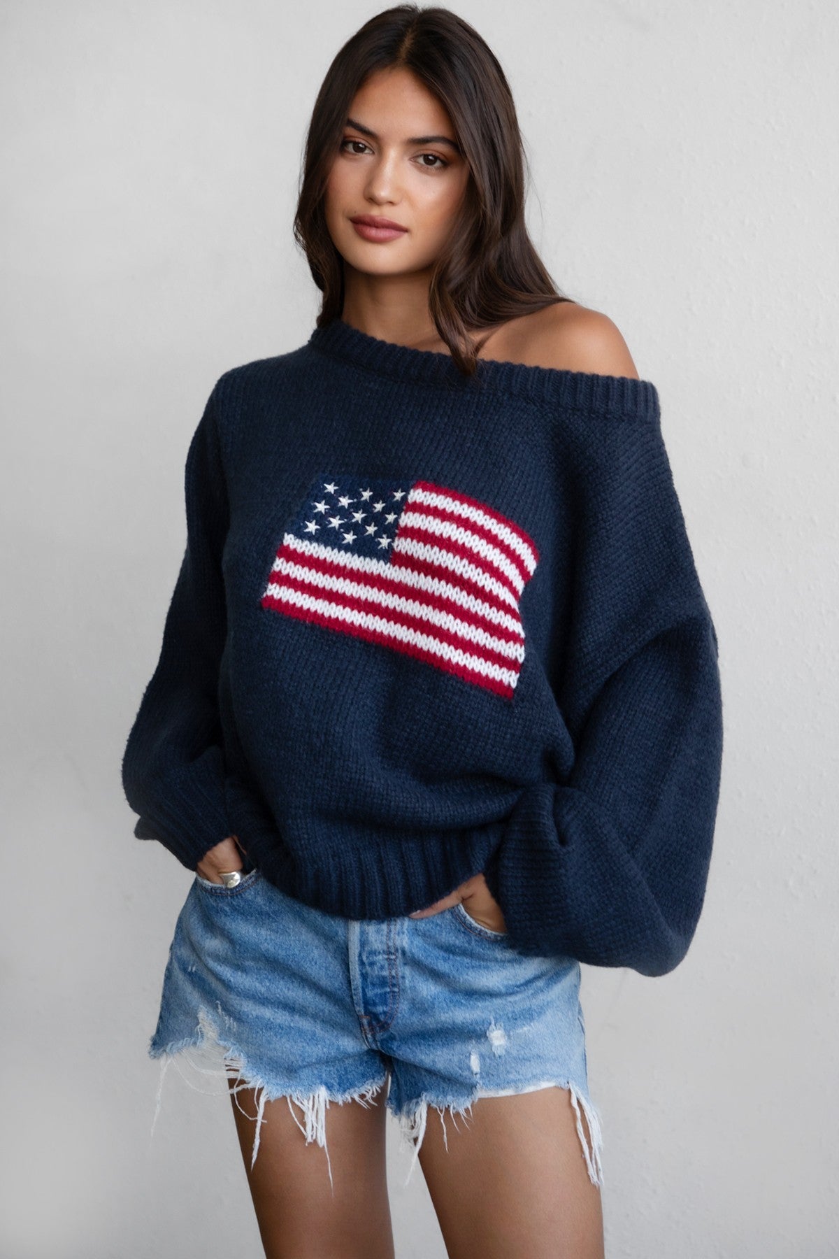 Woman wearing a TIC TOC BRANDI Ribbed Knit Sweater in navy with off-the-shoulder boat neck, American flag pattern, and semi-oversized fit with denim shorts.