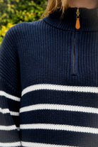 Woman wearing MAUREEN classic oversized striped half zip sweater featuring a timeless stripe pattern, half zip mock neckline with faux leather zipper pull, relaxed drop shoulder silhouette, chunky cotton sweater knit, textured rib stitching, and ribbed cuffs and hem for cozy coastal styling.