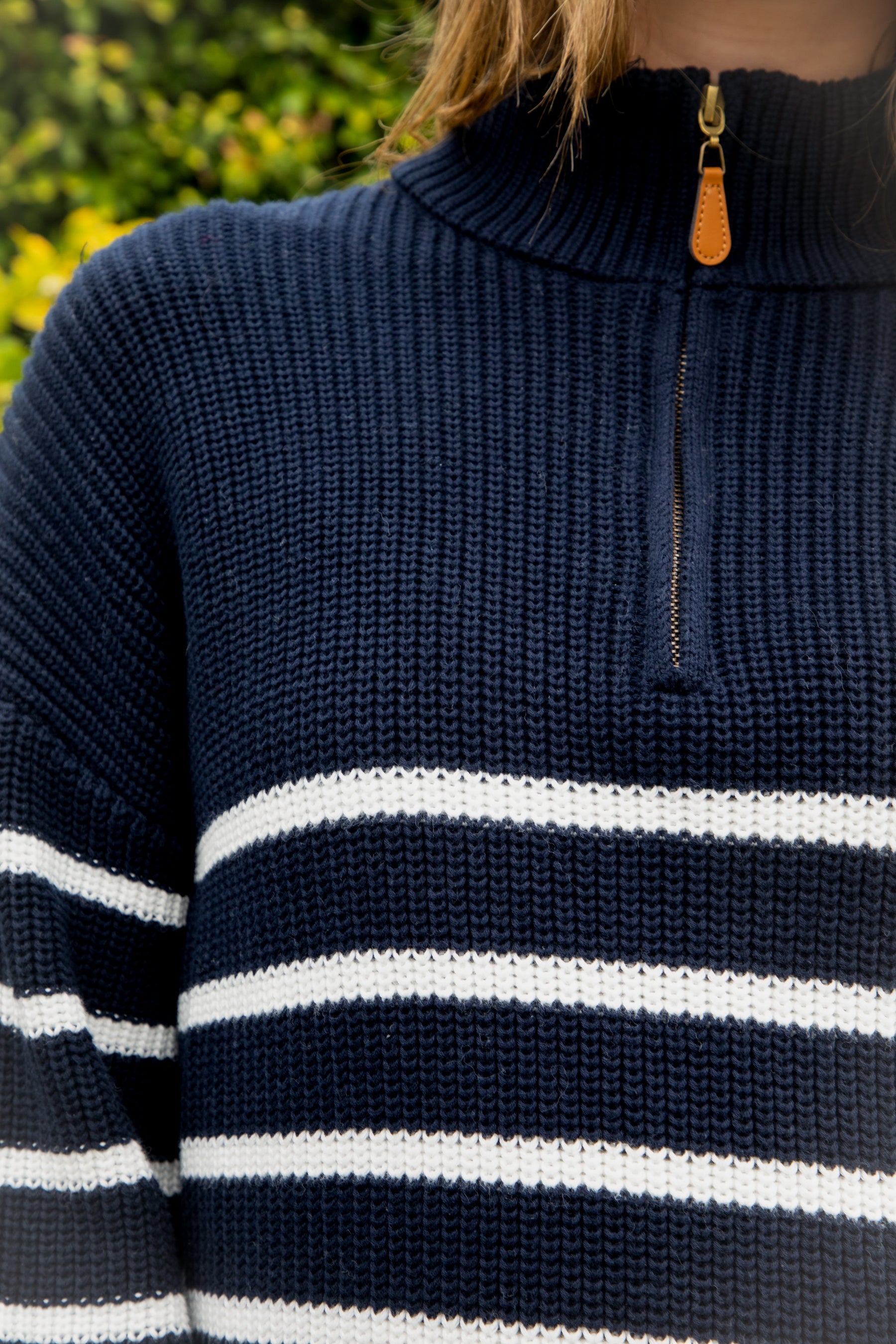 Woman wearing MAUREEN classic oversized striped half zip sweater featuring a timeless stripe pattern, half zip mock neckline with faux leather zipper pull, relaxed drop shoulder silhouette, chunky cotton sweater knit, textured rib stitching, and ribbed cuffs and hem for cozy coastal styling.