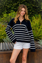 Woman wearing MAUREEN classic oversized striped half zip sweater featuring a timeless stripe pattern, half zip mock neckline with faux leather zipper pull, relaxed drop shoulder silhouette, chunky cotton sweater knit, textured rib stitching, and ribbed cuffs and hem for cozy coastal styling.