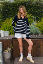 Woman wearing MAUREEN classic oversized striped half zip sweater featuring a timeless stripe pattern, half zip mock neckline with faux leather zipper pull, relaxed drop shoulder silhouette, chunky cotton sweater knit, textured rib stitching, and ribbed cuffs and hem for cozy coastal styling.