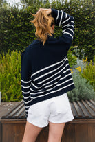 Woman wearing MAUREEN classic oversized striped half zip sweater featuring a timeless stripe pattern, half zip mock neckline with faux leather zipper pull, relaxed drop shoulder silhouette, chunky cotton sweater knit, textured rib stitching, and ribbed cuffs and hem for cozy coastal styling.