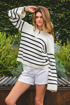 Woman wearing MAUREEN classic oversized striped half zip sweater featuring a timeless stripe pattern, half zip mock neckline with faux leather zipper pull, relaxed drop shoulder silhouette, chunky cotton sweater knit, textured rib stitching, and ribbed cuffs and hem for cozy coastal styling.