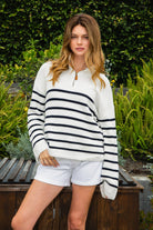 Woman wearing MAUREEN classic oversized striped half zip sweater featuring a timeless stripe pattern, half zip mock neckline with faux leather zipper pull, relaxed drop shoulder silhouette, chunky cotton sweater knit, textured rib stitching, and ribbed cuffs and hem for cozy coastal styling.