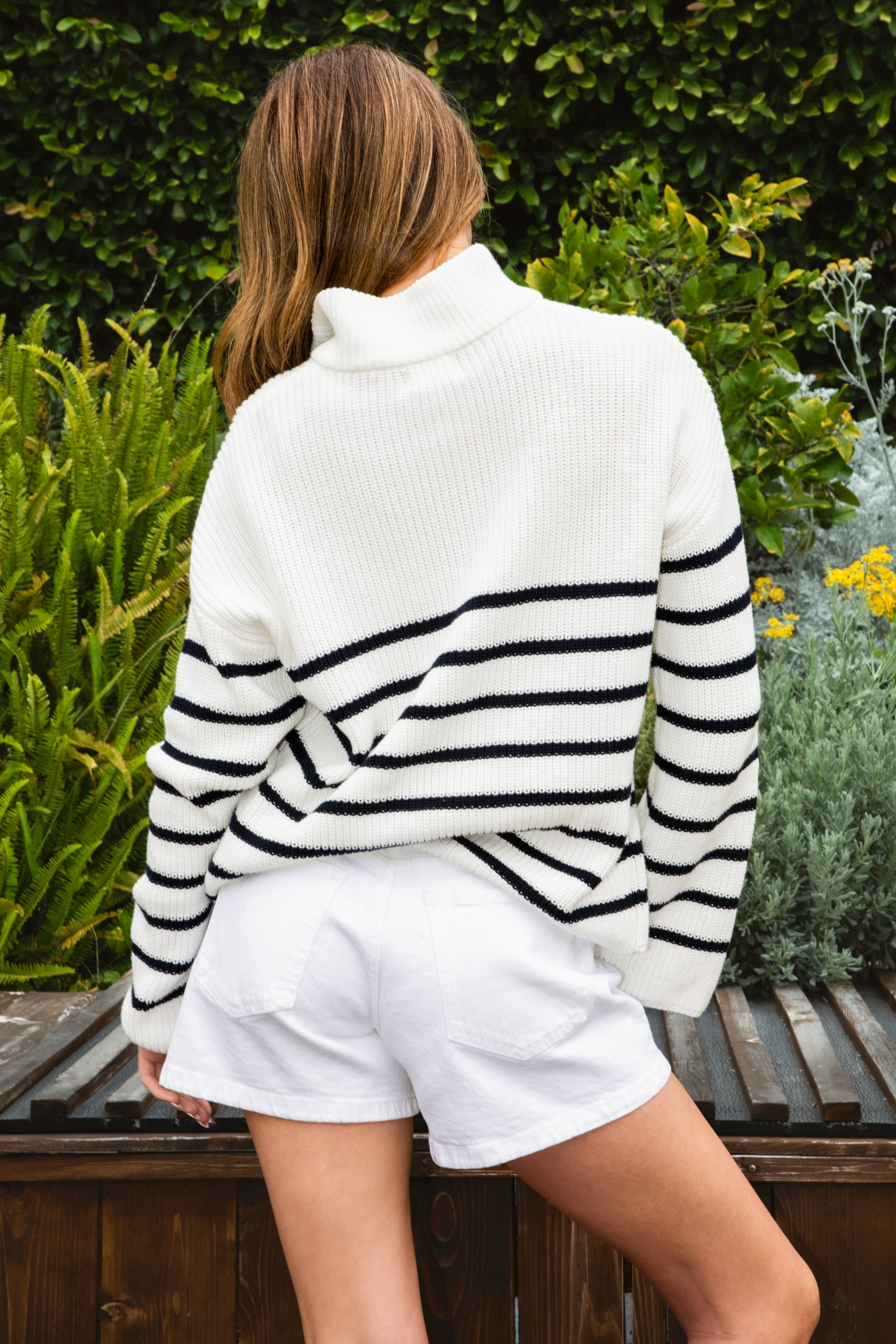 Woman wearing MAUREEN classic oversized striped half zip sweater featuring a timeless stripe pattern, half zip mock neckline with faux leather zipper pull, relaxed drop shoulder silhouette, chunky cotton sweater knit, textured rib stitching, and ribbed cuffs and hem for cozy coastal styling.