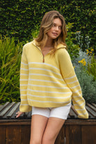 Woman wearing MAUREEN classic oversized striped half zip sweater featuring a timeless stripe pattern, half zip mock neckline with faux leather zipper pull, relaxed drop shoulder silhouette, chunky cotton sweater knit, textured rib stitching, and ribbed cuffs and hem for cozy coastal styling.