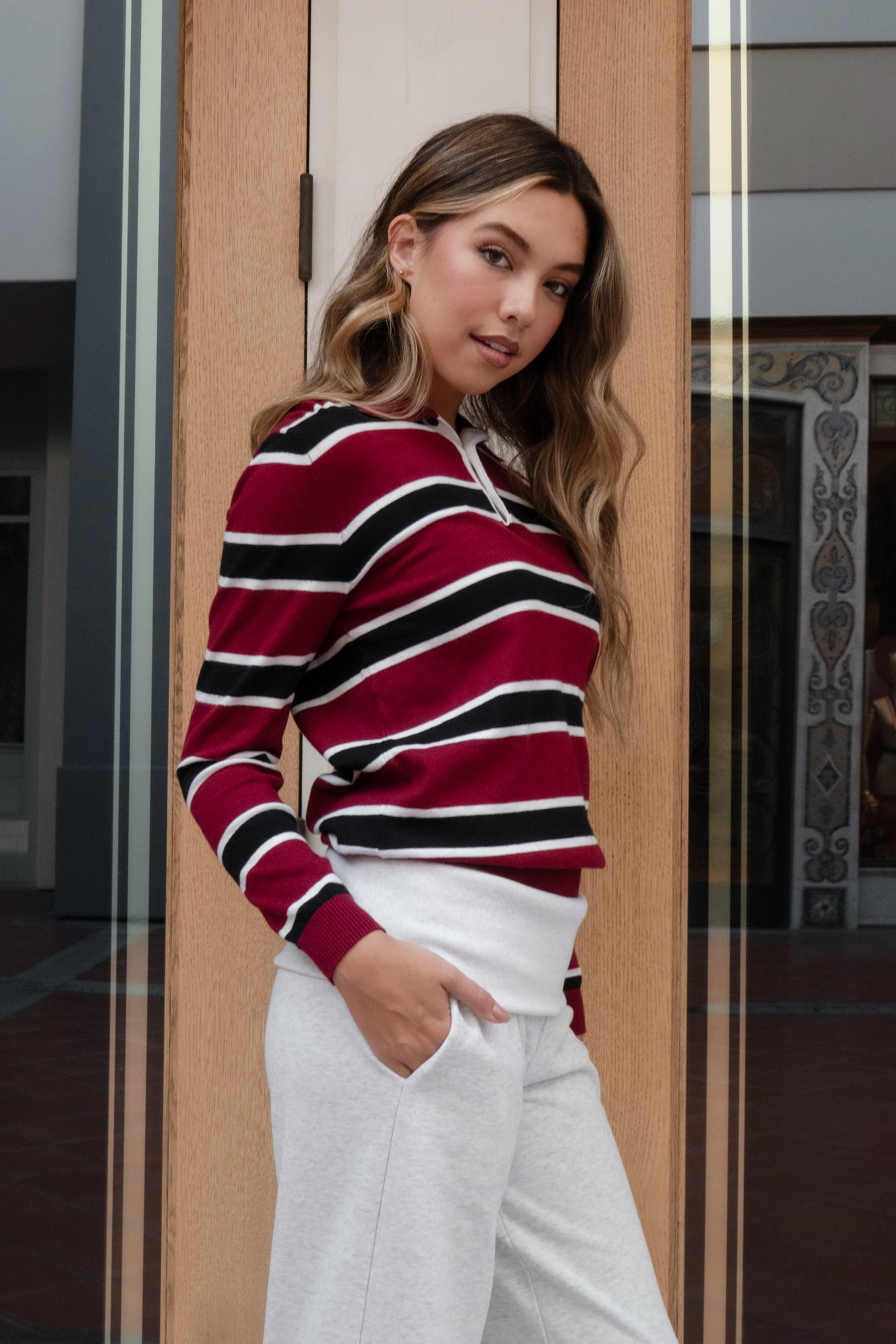 woman wearing TIC TOC TC30738 RHODES striped polo T-shirt featuring a relaxed collar, quarter button-up closure, multicolor stripe pattern, and smooth sweater knit texture styled casually with denim in an outdoor lifestyle setting.