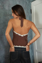 Woman wearing a brown polka dot top with lace details and dark jeans against a neutral background.
