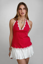 Woman wearing a red polka dot top with white lace trim on a gray background