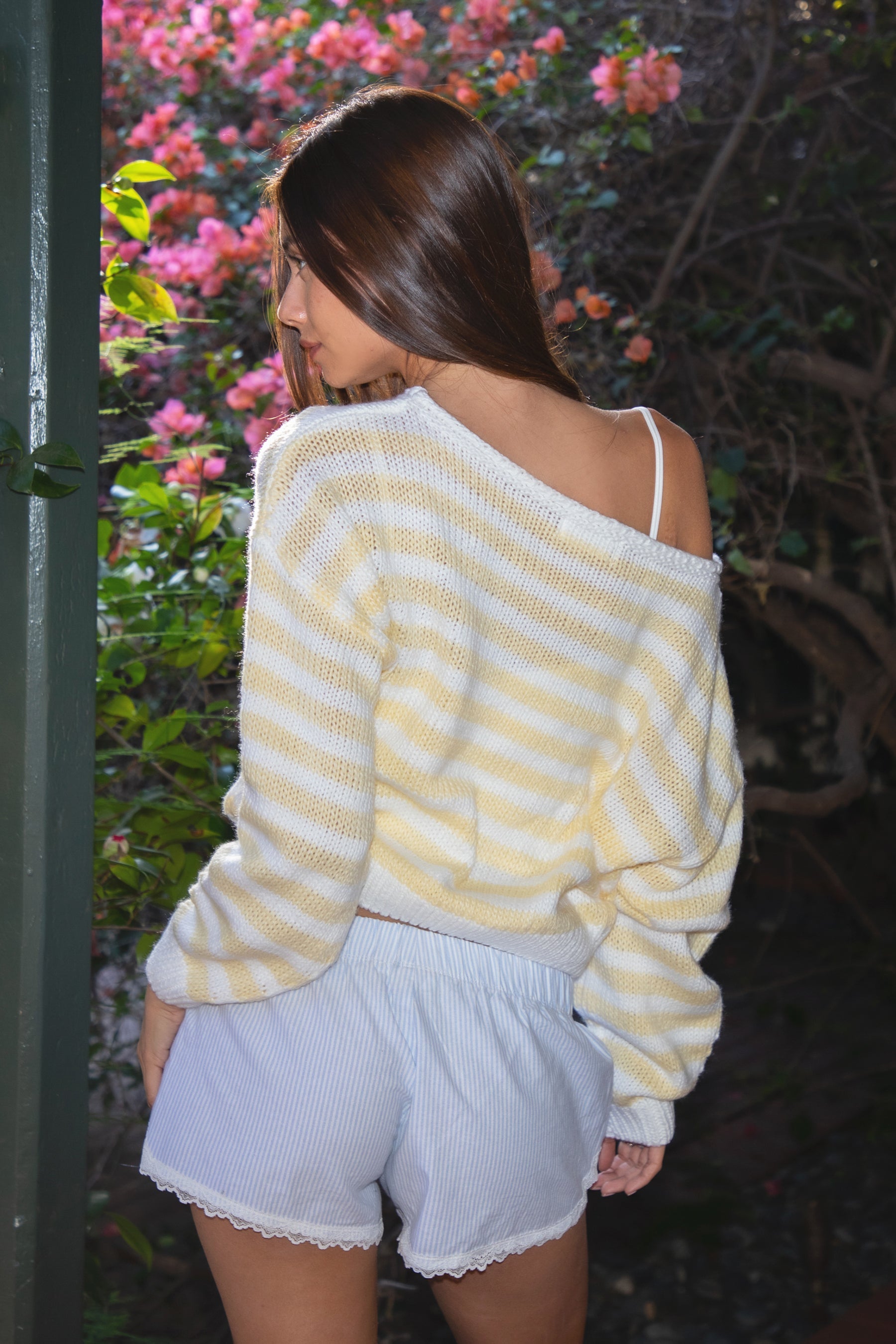 Woman wearing TIC TOC TC31201 PAISEY striped knit off the shoulder oversized sweater with rugby color block pattern inblush and cream paired with a white mini skirt in an outdoor setting. 