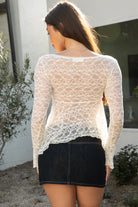 Woman wearing TIC TOC TC31594-ROSELLE ROSELLE lace top featuring soft stretch lace fabric, a delicate scalloped V-neckline, long fitted sheer sleeves, a romantic airy babydoll silhouette with lightweight semi-sheer body, and a softly flared draped hemline, styled with high-rise bottoms for a feminine date-night look.