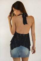 Woman wearing TIC TOC TC31623 LOVELLE deep V-neck lace halter top in black, featuring a plunging neckline, fitted lined bust, sheer lace body, and asymmetrical handkerchief hem, styled with a vintage wash denim mini skirt for a feminine Y2K-inspired look.