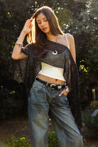 Woman wearing TIC TOC TC31650-SOLENA SOLENA crystal sequin crochet poncho featuring lightweight open crochet knit fabric, allover crystal sequin embellishments, a wide off-shoulder neckline, relaxed draped poncho silhouette, cropped asymmetrical hem, and thin tassel fringe detail, styled over a fitted inner layer for a western festival and vacation-ready look.