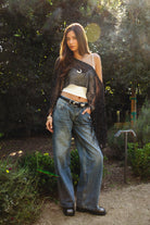 Woman wearing TIC TOC TC31650-SOLENA SOLENA crystal sequin crochet poncho featuring lightweight open crochet knit fabric, allover crystal sequin embellishments, a wide off-shoulder neckline, relaxed draped poncho silhouette, cropped asymmetrical hem, and thin tassel fringe detail, styled over a fitted inner layer for a western festival and vacation-ready look.